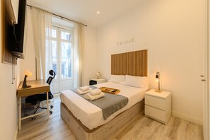 Habitación de hotel con cama, escritorio, silla, mesita de noche, televisor y ventana con cortinas.