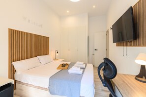 A modern hotel room with a bed, bedside table, TV, and a wooden headboard.