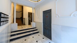Un grand escalier en marbre, avec une porte sombre qui mène à un couloir éclairé par un luminaire circulaire.