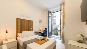 Une chambre d’hôtel moderne équipée d’un lit, d’une table de chevet, d’un bureau, d’une chaise et d’un balcon avec vue.