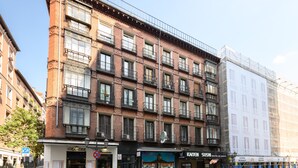 Un immeuble à plusieurs étages avec une façade en briques, des devantures de magasins, dont un restaurant de sushis, et un espace de stationnement pour vélos bien visible.
