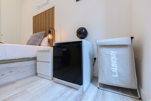 Un dormitorio con una cama, un electrodoméstico pequeño negro, una cesta de ropa blanca y un globo terráqueo colgado en la pared.