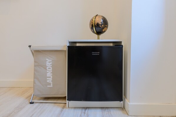 Une pièce compacte et moderne, dotée d’un réfrigérateur noir, d’un petit globe décoratif et d’un sac à linge.