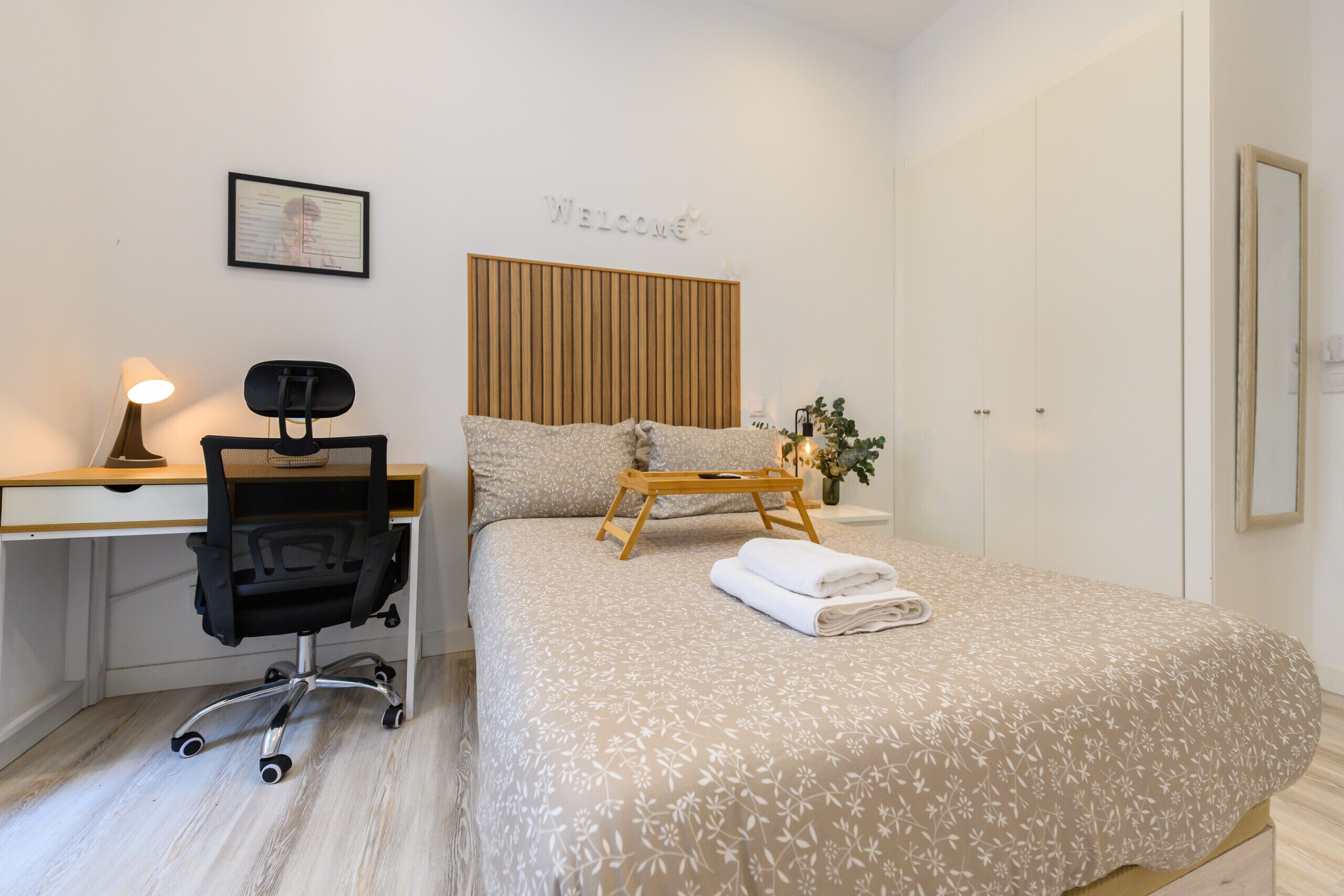 Een netjes opgemaakte slaapkamer met een bed, een bureau, een stoel en een nachtkastje.