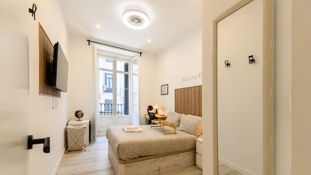 Une chambre à coucher moderne avec un lit, une table de chevet et un téléviseur fixé au mur.