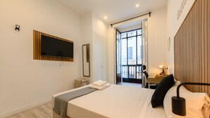A modern hotel room with a large bed, a flat-screen TV mounted on the wall, a bedside table with a lamp, and a view of the outside balcony. - Zurich: room with comfort and shared areas Gran Vía-Madrid (Madrid)