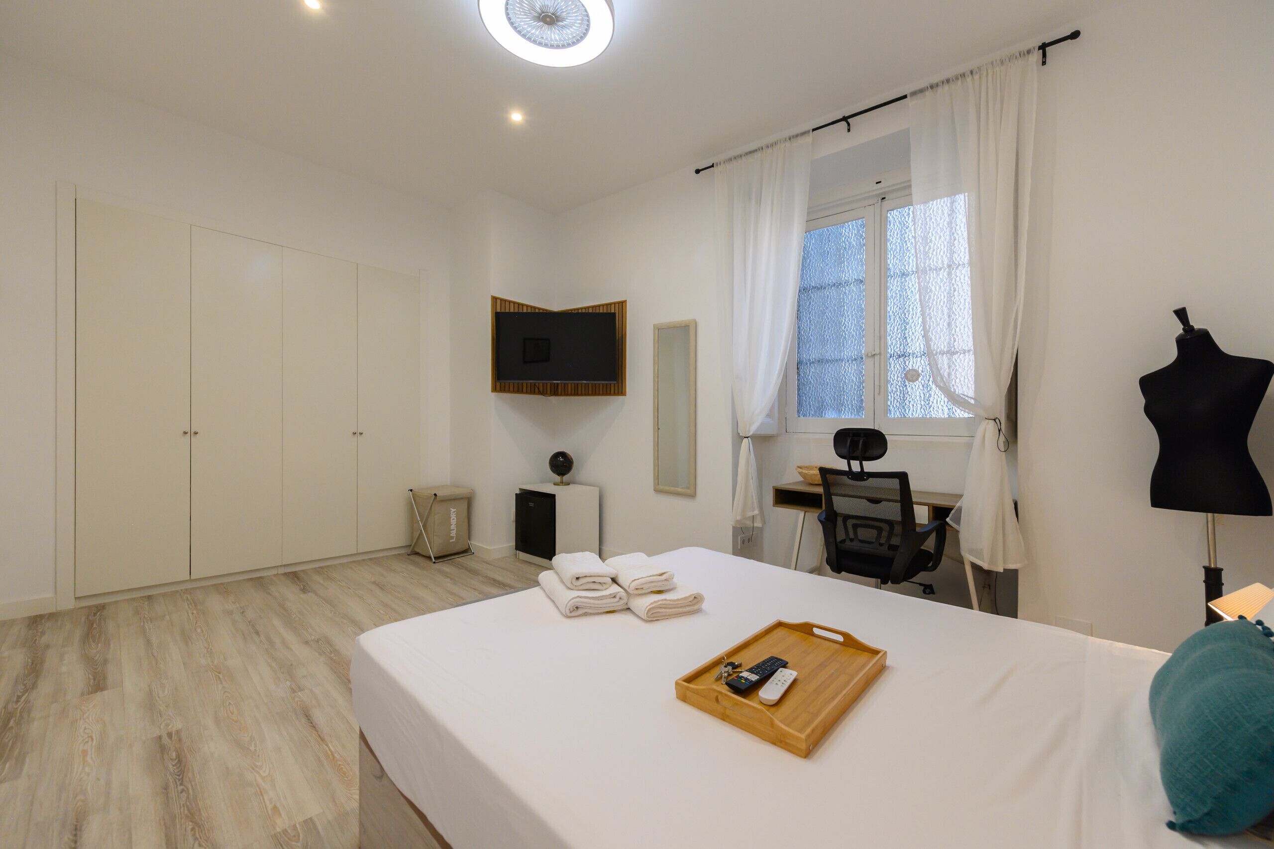 Hotelkamer met een bed, een bureau, een stoel, een televisie, een kledingkast en een raam met gordijnen.