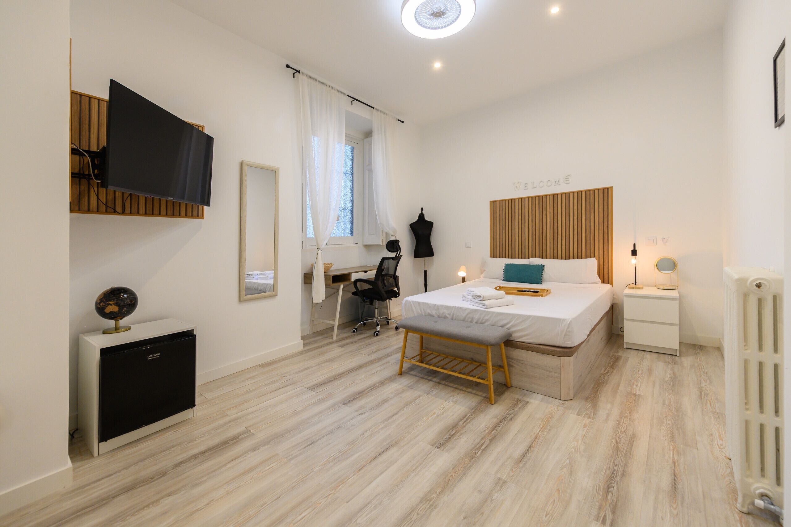 Un dormitorio moderno con cama, mesita de noche, lámpara y un escritorio con silla.
