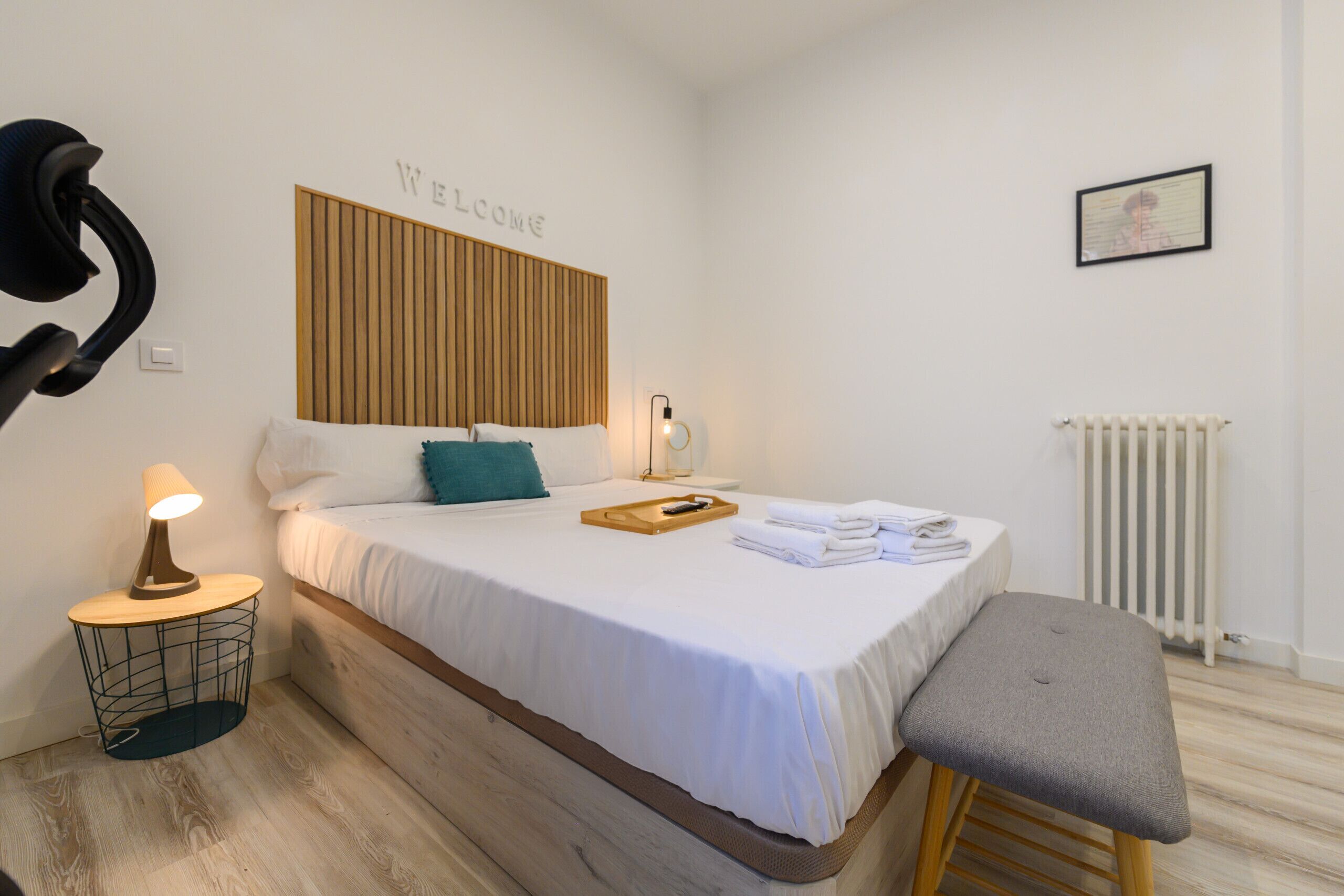 Un dormitorio ordenado con cama, mesita de noche y un banco.
