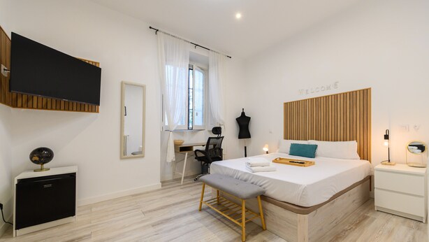 Une chambre moderne comprenant un lit, une table de chevet, un bureau, une chaise et un téléviseur fixé au mur.