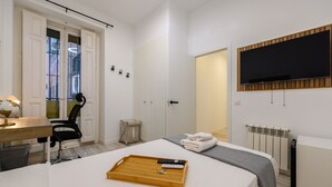 Habitación de hotel con cama, escritorio con silla, televisión montada en la pared y radiador.
