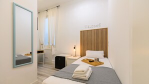 A modern hotel room with a bed, a desk, a chair, a wardrobe, and a mirror.