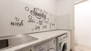 A modern laundry room with a built-in washing machine and dryer, a stainless steel sink, and decorative wall tiles with laundry-related phrases.