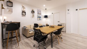 Une pièce moderne et bien éclairée, avec une table à manger en bois, des chaises noires, un canapé beige et une petite table d’appoint avec une lampe.