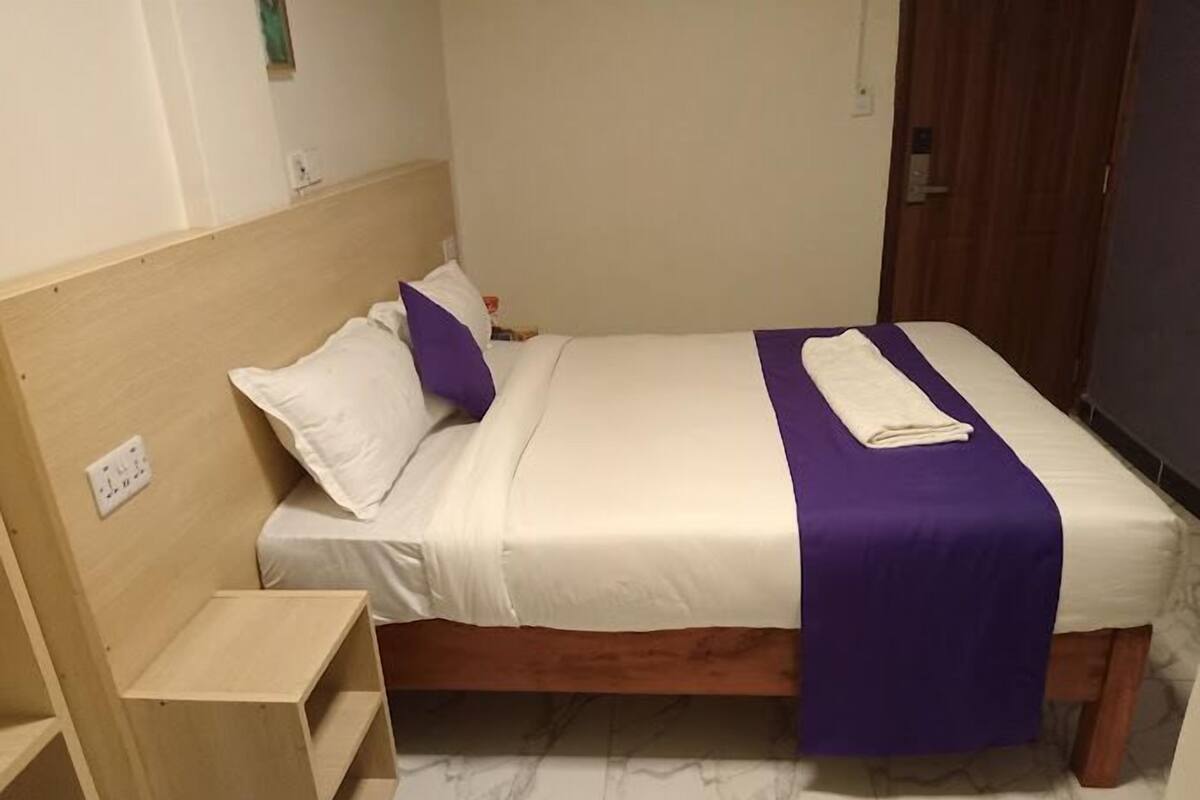 Una cama individual con cabecera de madera, ropa de cama blanca y un toque de color púrpura.