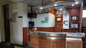 A reception area with a curved wooden counter, a framed portrait, and a small shelf with certificates. - Hotel Citymax Nakuru (Nakuru)