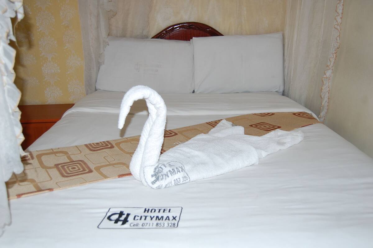 Una cama de hotel con una toalla con forma de cisne y una tarjeta con el nombre del hotel.