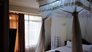 A four-poster canopy bed with white linens, a wooden headboard, and a nightstand with a lamp. - Hotel Citymax Nakuru (Nakuru)
