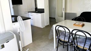 A compact kitchen with white cabinets, a black countertop, and a built-in microwave. There is a dining area with a table and chairs, and a door leading to another room.