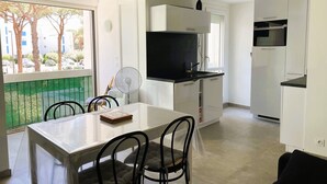 A modern kitchen with white cabinets, a black countertop, and a built-in oven. There is a dining table with chairs and a fan near the window.