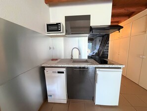 Ett kompakt kök med en inbyggd mikrovågsugn, en fläktkåpa i rostfritt stål, en diskmaskin och en diskho.