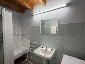 Une salle de bain avec un lavabo blanc, un miroir, une douche et un sol carrelé.