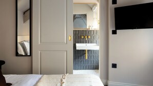 A hotel room with a bed, a mirror, a TV, and a bathroom with a sink and tiles. - Domain Boutique Rooms (Lancaster)