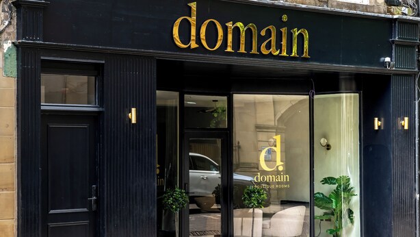 A boutique hotel entrance with a black facade, glass doors, and potted plants. - Domain Boutique Rooms (Lancaster)