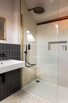 Un baño moderno con ducha envuelta en vidrio, un lavabo blanco y un pequeño estante con artículos de tocador.
