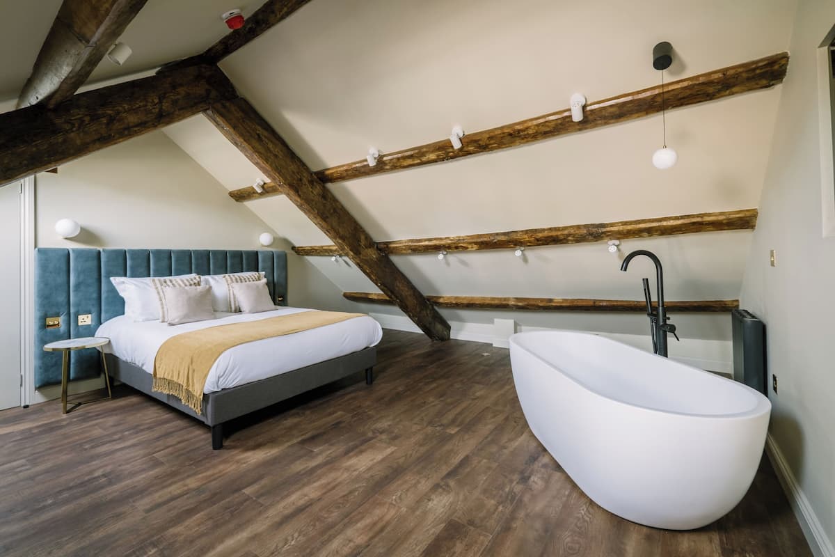 A bedroom with a large bed, a bathtub, wooden beams, and a sloped ceiling.