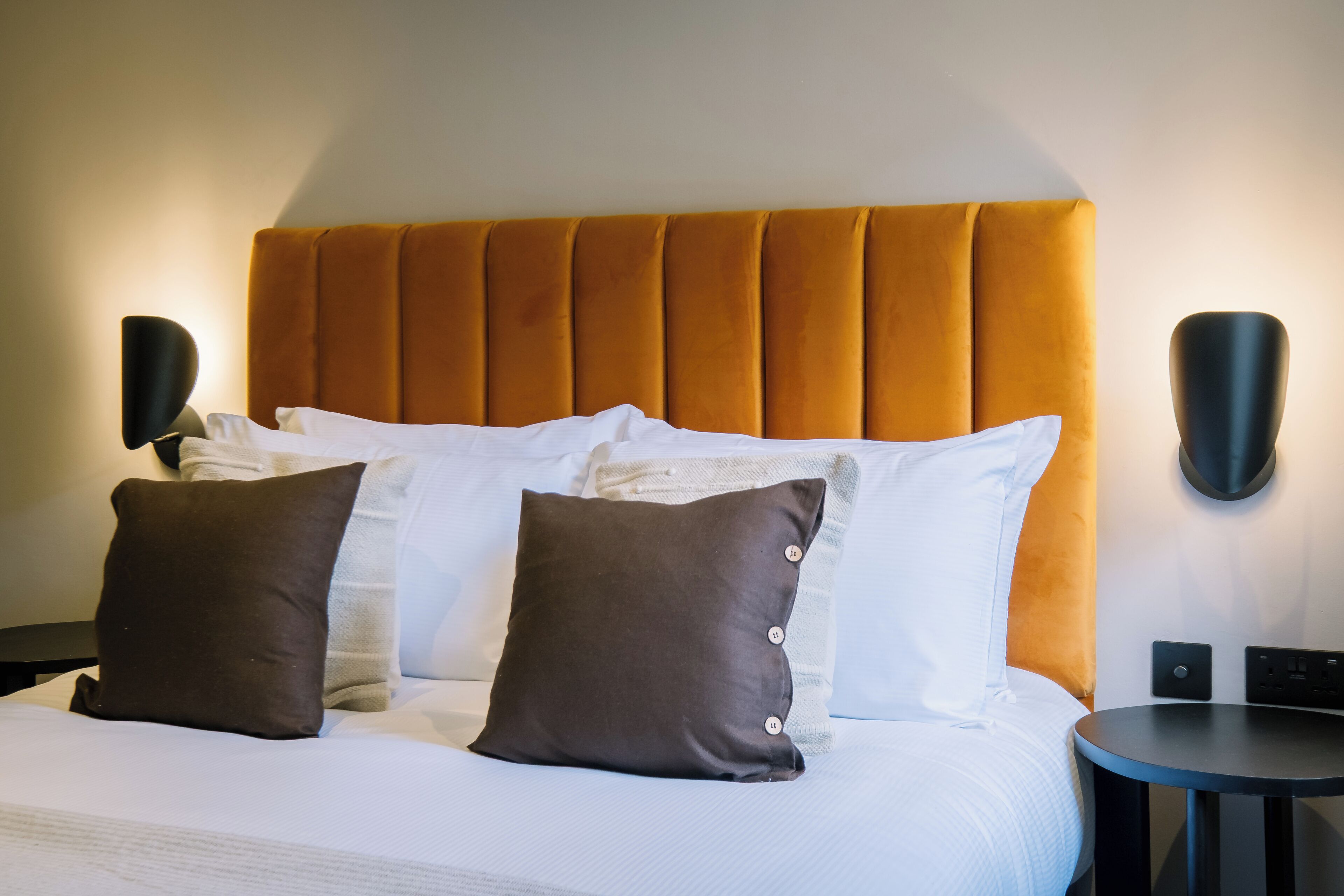 A hotel room with a large bed, two pillows, a headboard, bedside tables, and wall-mounted lamps.