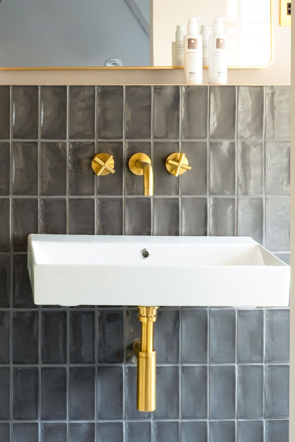 A bathroom with a white sink, gold fixtures, and a tiled backsplash.