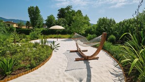 A hammock on a sandy path surrounded by greenery, with a clear sky and distant mountains. - Villa Forte dei Marmi Pool & Garden (Forte dei Marmi)