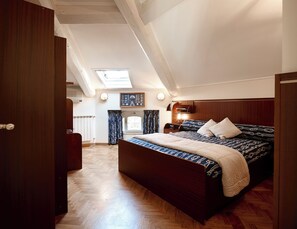 Un dormitorio con una cama grande, suelo de madera, un tragaluz e imagen enmarcadas en la pared.