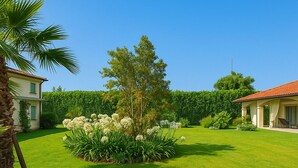 A well-maintained lawn with a central tree and flower bed, surrounded by a hedge and two buildings with red roofs. - Villa Forte dei Marmi Pool & Garden (Forte dei Marmi)