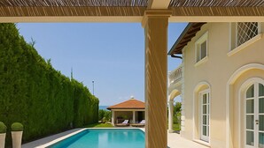 A pool area with a wooden table, a vase with flowers, and a view of a house with a pool and a gazebo. - Villa Forte dei Marmi Pool & Garden (Forte dei Marmi)