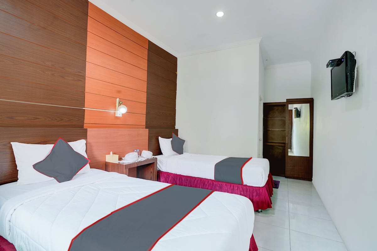 Une chambre d’hôtel avec deux lits, un mur décoratif en bois, un téléviseur à écran plat et une petite table avec un téléphone et une bouteille d’eau.