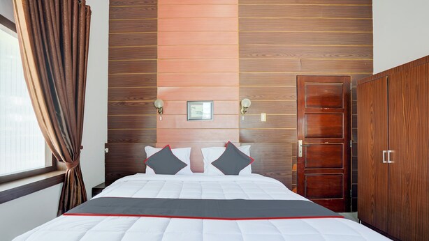 Un lit bien fait, avec une couette blanche rehaussée d’une touche de rouge, une tête de lit en bois, une armoire en bois et un tableau encadré accroché au mur.