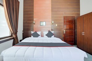 Un lit bien fait, avec une couette blanche rehaussée d’une touche de rouge, une tête de lit en bois, une armoire en bois et un tableau encadré accroché au mur.