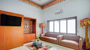 Un salon avec un canapé, un téléviseur fixé sur un meuble en bois, un ventilateur et une fenêtre donnant sur un paysage agréable.