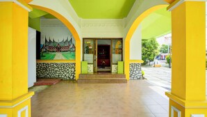 Un hall d’hôtel avec un sol carrelé, des colonnes jaunes et blanches, un mur en pierre et une fresque représentant un bâtiment traditionnel.