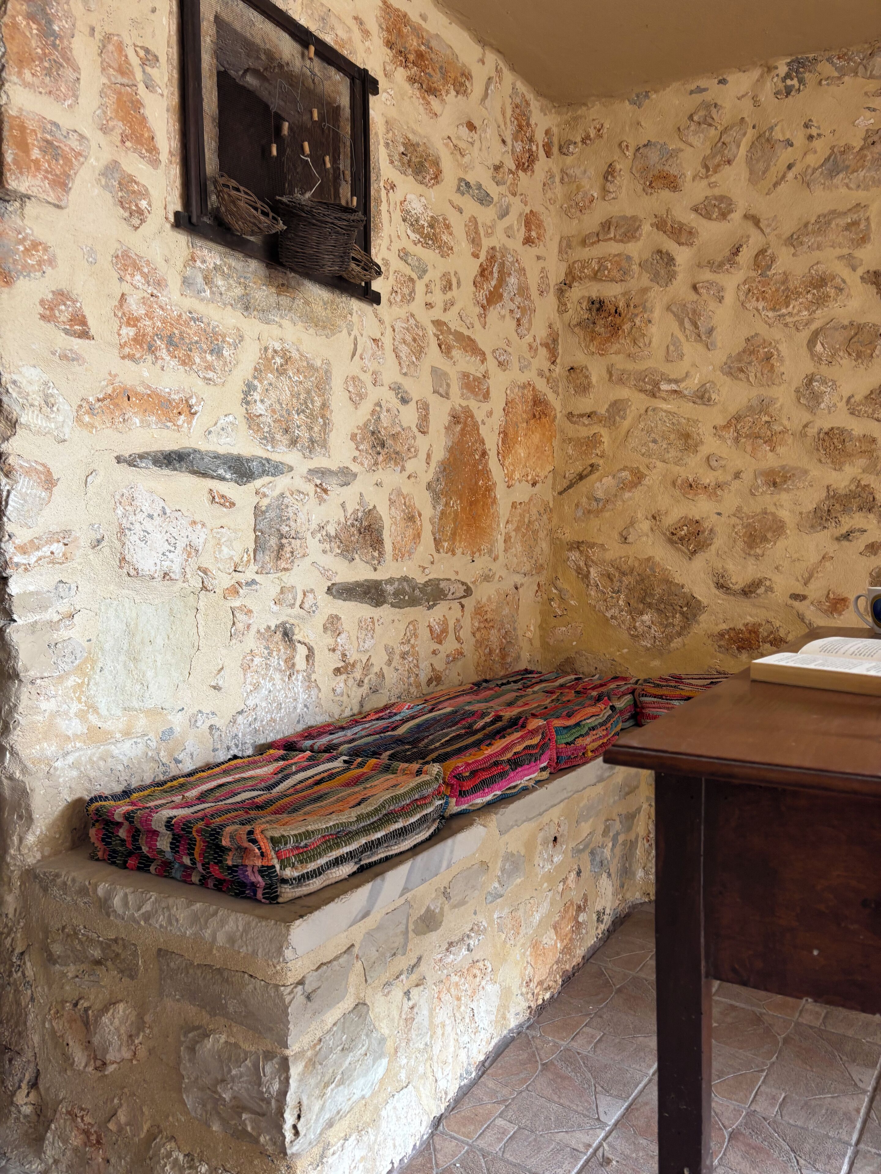 A stone wall with a woven bench and a wooden table with a book.