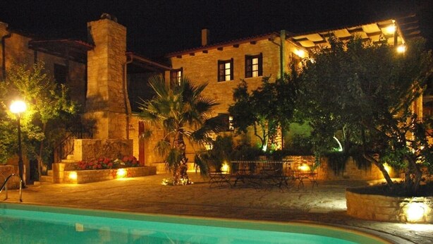 A pool area with a stone building in the background, surrounded by trees and outdoor seating. - Electra Stone Suite  (Roumeli)