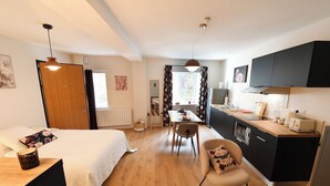 A modern bedroom with a bed, bedside table, and a chair. There is a kitchen area with a counter, stove, and cabinets. - ALBARINE la Source river/lakes, waterfalls and mountains, plastics processing business (Arbent)