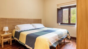 A bedroom with a wooden bed, a bedside table with a lamp, and a window with a view of trees. - Rifugio Giuliano Marini (Petralia Sottana)