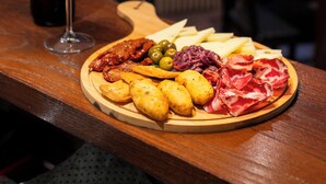 A wooden table with a charcuterie board, a bottle of wine, and a glass of red wine. - Rifugio Giuliano Marini (Petralia Sottana)