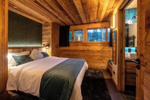 A wooden cabin bedroom with a bed, a window, and a bathroom visible through an open door. - Chalet WHA – Pied des pistes à la Clusaz, 12 pers, jacuzzi, hammam, gym (La Clusaz)