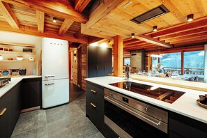 A modern kitchen with wooden beams, a white refrigerator, black cabinets, and a large island with a sink. - Chalet WHA – Pied des pistes à la Clusaz, 12 pers, jacuzzi, hammam, gym (La Clusaz)