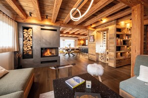 A cozy living room with a fireplace, wooden beams, a dining area, and a bookshelf. - Chalet WHA – Pied des pistes à la Clusaz, 12 pers, jacuzzi, hammam, gym (La Clusaz)