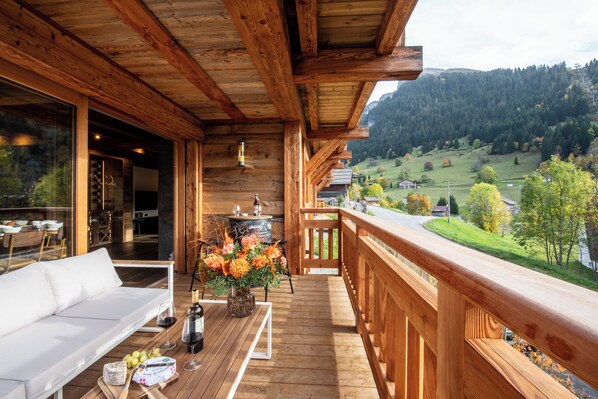 A wooden deck with a sofa and dining table, a view of a valley, and a wooden railing. - Chalet WHA – Pied des pistes à la Clusaz, 12 pers, jacuzzi, hammam, gym (La Clusaz)